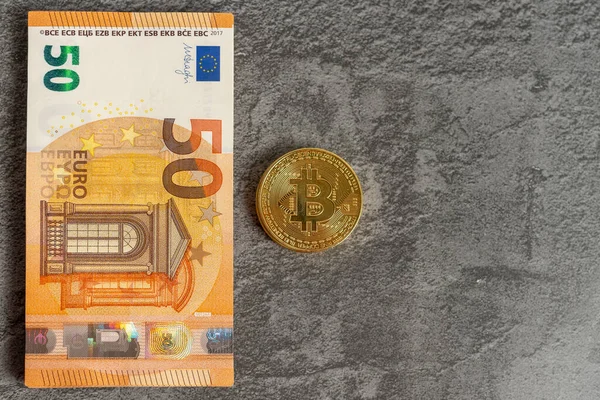 Top view of bitcoin coin next to several euro banknotes on a gray background. Concept of investments in new virtual currencies. Copy Space