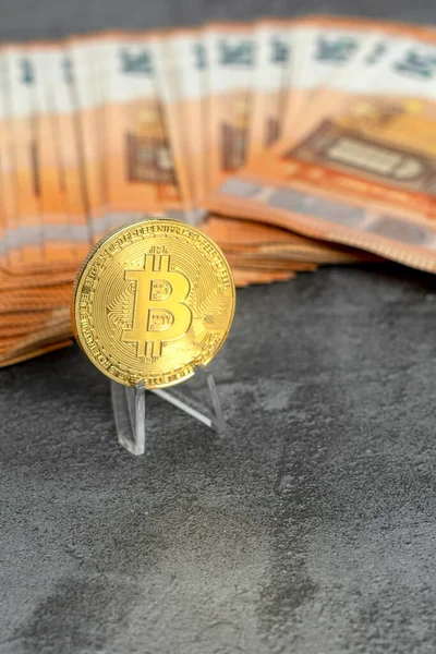 Bitcoin coin next to several euro banknotes on a gray background. Concept of investments in new virtual currencies. Copy Space