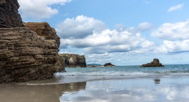 Kuzey İspanya 'daki Las Catedrales' in sakin sahillerinde bulutlar ve dev taşlarla dolu güzel mavi bir gökyüzü..