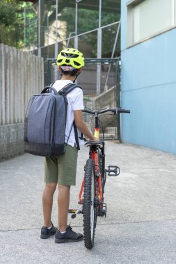 Bisikleti ve sırt çantasıyla okula gelen çocuk bisikleti park etmeye hazır. Okul konseptine dönelim. 