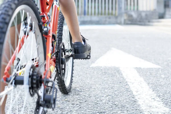 Blisko dzieci nogi zamontowane na rowerze gotowy do jazdy obok białego znaku strzałki namalowane na ziemi wskazując przed siebie. Koncepcja Kontynuuj — Zdjęcie stockowe