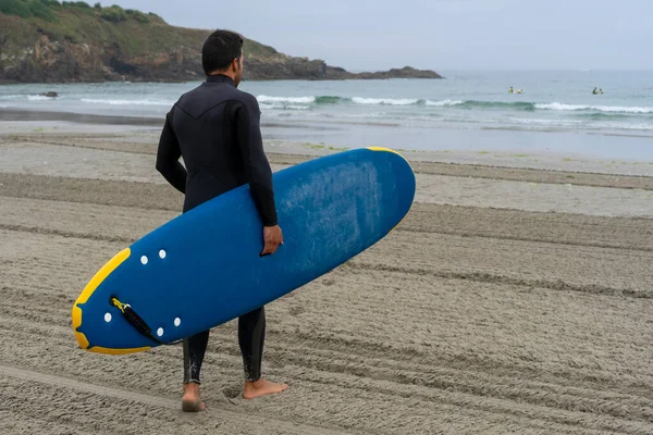 Egy szörfös búvárruhában megfigyeli az Atlanti-óceán partjait, és szörfdeszkával készül szörfözni.. — Stock Fotó