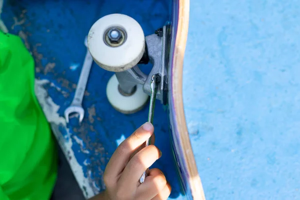 Close up de uma criança reparando a roda de seu skate depois de usá-lo no parque de skatistas. — Fotografia de Stock