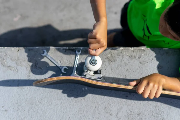 Vista dall'alto di un bambino concentrato che ripara il suo skateboard prima di utilizzarlo all'interno dello skateboard park in una giornata di sole. — Foto Stock