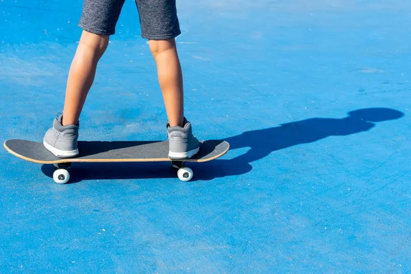 Close up de pernas de um menino em um skate em um fundo azul mostrando a sombra de seu corpo no chão. — Fotografia de Stock