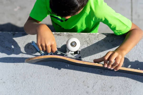 Ovanifrån av en pojke som reparerar hjulet på sin skateboard efter att ha använt den inne i skateboard park på en solig dag. — Stockfoto