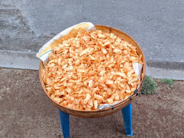 Cassava cipsleri dışarıda yuvarlak bir bambu kabında kurutuluyor, doğal ışık altında altın çıtır çıtır dokuları gösteriyor, kırsal alanda geleneksel bir yemek hazırlama süreci..