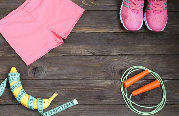 Sports apparel, skipping rope, banana and measuring tape on wooden background .Sport, diet and healthy lifestyle concept. Clothing, equipment and fitness accessories. The place to advertise.