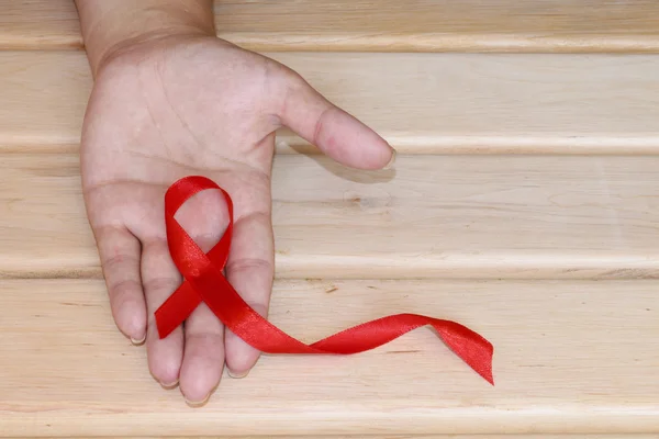 Symbolické pojetí Světový den boje proti Aids. Červenou stužku v rukou mladé ženy na dřevěné pozadí. — Stock fotografie