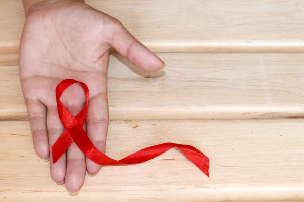 De symbolische voorstelling van de Werelddag voor Aids-bestrijding. Het rode lint in de handen van een jonge vrouw op houten achtergrond. — Stockfoto