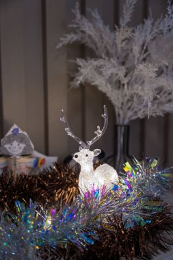 Aydınlatılmış rengarenk ren geyiği figürü gerçek bir evin içinde renkli süslemeler ve donmuş yapay dallar arasına yerleştirilip sıcak ve şenlikli bir kış atmosferi yaratıyor..