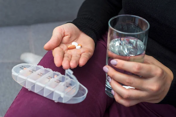 A female going to take tablets from pill box. A woman takes medicine with a glass of water. Pharmacy and healthcare concept.