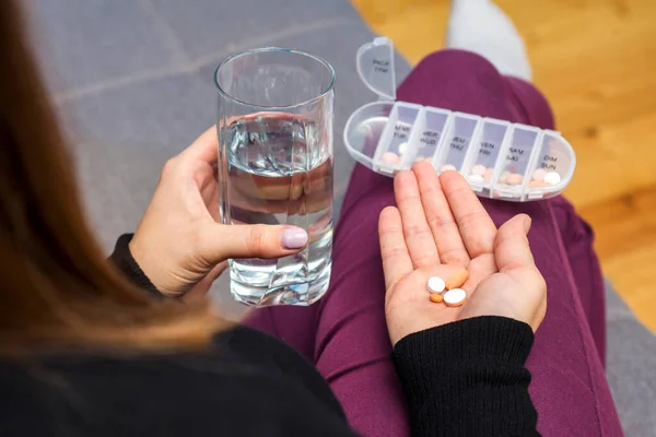 A female going to take tablets from pill box. A woman takes medicine with a glass of water. Pharmacy and healthcare concept.