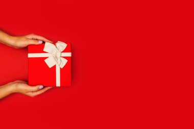 Kadının elinde kırmızı bir hediye kutusuyla kurdeleyle bağlanmış bir görüntü var. Noel, Yeni Yıl, Sevgililer Günü veya Yıldönümü hediyesi.