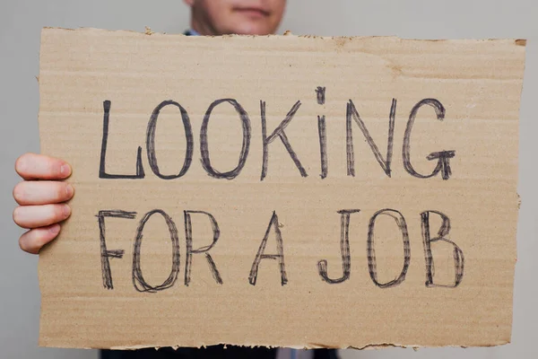 隔離のために職を失った若いビジネスマンが仕事を探しています ビジネスマンは 仕事を探しているテキストと段ボールの看板を保持しています 失業成長の概念 — ストック写真