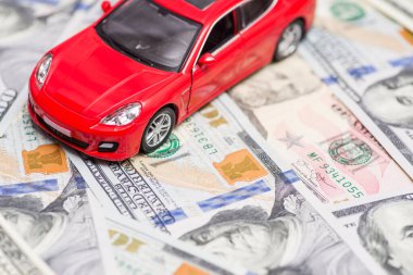 Kırmızı oyuncak araba dolar banknotlarının üzerinde duruyor. Araba, yakıt, sigorta ve diğer araba maliyetleri.