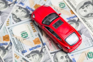 Kırmızı oyuncak araba dolar banknotlarının üzerinde duruyor. Araba, yakıt, sigorta ve diğer araba maliyetleri.