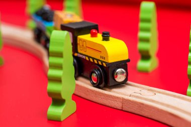 Demiryolundaki tahta oyuncak treni kırmızı arka plandaki yeşil ağaçların arasında. Anaokulu ve anaokulu çocuğu için eğitici oyuncaklar.
