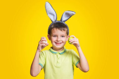 Tavşan kulaklı sevimli çocuk sarı arka planda renkli yumurtaları elinde tutuyor. Paskalya yumurtaları ve sarı arka planda tavşan kulakları olan mutlu çocuk..