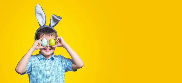 Roztomilý Chlapec Králičími Ušima Drží Barevná Vejce Blízkosti Očí Žlutém — Stock fotografie