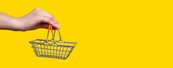 ショッピングコンセプト 女性の手は黄色の背景におもちゃの金属ショッピングバスケットを保持しています 広告のコピースペース — ストック写真