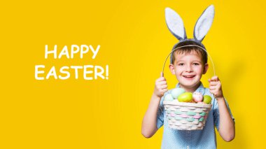 Elinde Paskalya sepeti ve kafasında sarı bir arka planda tavşan kulağı olan sevimli bir çocuk. Mutlu Paskalyalar.