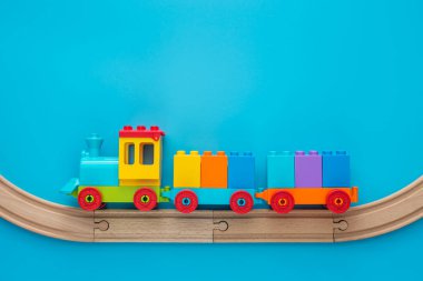Kopya alanı olan oyuncaklar. Çocuk oyuncak treni ahşap demiryolunda iki vagon ile mavi arka planda metin için fotokopi alanı ile.