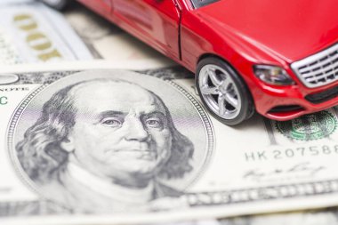 Red toy car on dollar bills. Cost of buying a car, fuel, insurance and other car costs. Rent, buy or insurance car concept.