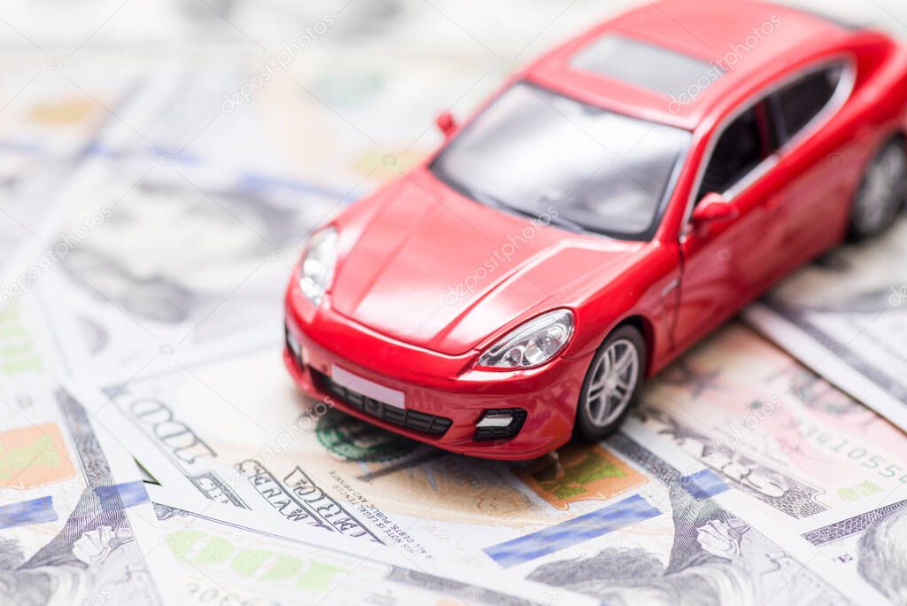 Red toy car on dollar bills. Cost of buying a car, fuel, insurance and other car costs. Rent, buy or insurance car concept.