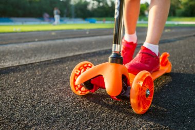 Bir çocuk mobilete biniyor. Renkli scooterlı çocuk. Çocuklar için açık hava eğlencesi. Çocuklar için yaz sporları.