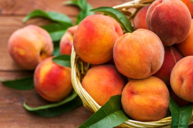 Tahta bir arka planda hasır sepette yaprakları olan taze sulu şeftaliler. Hasır sepette taze koparılmış şeftaliler..