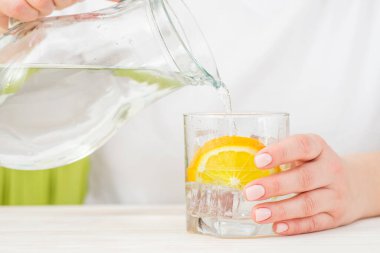 Dişi eller sürahide bulunan suyu limon ve buzla dolu cam bir şişeye döküyor. Sağlık ve diyet konsepti. Sıcak bir günde susuzluğunu gidermek..