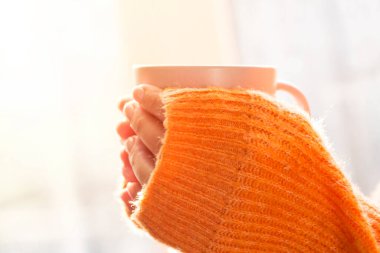 Sıcak içeceği olan kadın elleri. Turuncu kazaklı genç bir kadın elinde çay ya da kahve fincanı tutuyordu..