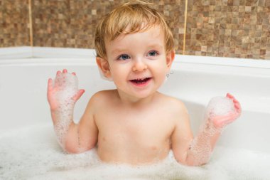 Mutlu çocuk küvette köpükle banyo yaparak eğleniyor. Güzel, mutlu çocuk banyo yaparken küvette sıçrıyor, bebek banyosu yapıyor..