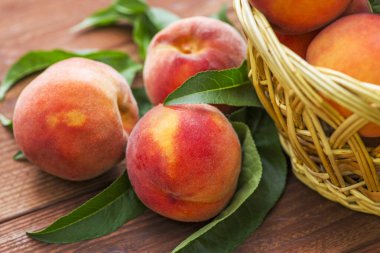 Tahta bir arka planda hasır sepette yaprakları olan taze sulu şeftaliler. Hasır sepette taze koparılmış şeftaliler..