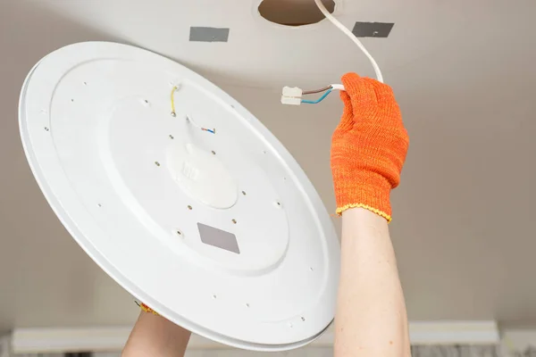 An electrician installs a chandelier on the ceiling. Hands of an electrician are installing and connecting a lamp to a ceiling. Ceiling lamp repair.