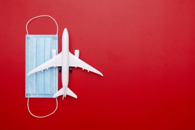 Kırmızı arka planda tıbbi maskesi olan bir uçak modeli. Karantina ve tecrit süresince güvenli uçuş ve seyahat. İyi yolculuklar. Sınırlar açılıyor.