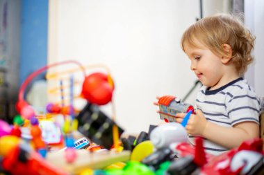Oyuncak çocuğun önünde bir sürü farklı ve renkli oyuncak. Küçük çocuk çocuk odasında oyuncak oynuyor..