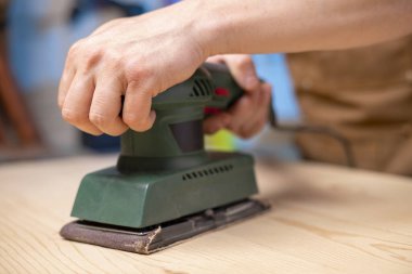 Marangoz, elektrikli zımparalama makinesiyle ahşap kalasları zımparalıyor. Bir marangoz zımpara makinesiyle odun öğütür..