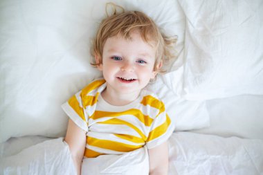 Sabahın erken saatlerinde beyaz yataktaki neşeli çocuk manzarası. Yakışıklı bir çocuğun portresi uyandı..