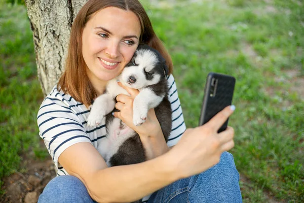 티셔츠를 강아지를 미녀는 공원에 사진이나 셀카를 핸드폰으로 찍거나 사진을 찍는다 — 스톡 사진