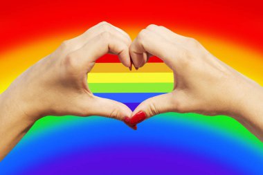 Gay gurur konsepti. Kadınların elleri gay gururu LGBT gökkuşağı bayrağıyla kalp işareti yapıyor.