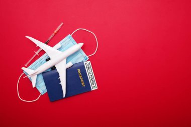 Şırınga, oyuncak uçak, tıbbi maske ve kırmızı arka planda 'Covid-19' yazılı test edilmiş pasaport. Covid-19 salgını sırasında seyahat kavramı.