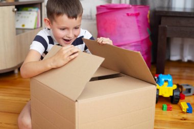 A boy is unpacking cardboard box ( gift box or parcel) at home. Delivery and service concept. Online shopping. clipart