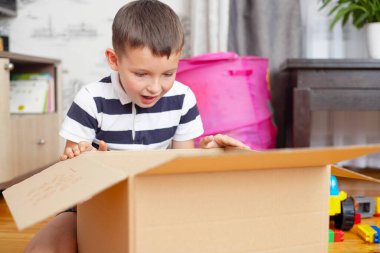 Bir çocuk evde karton kutu (hediye kutusu veya paket) açıyor. Teslimat ve servis konsepti. İnternetten alışveriş.