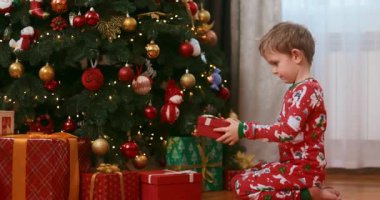 Güzel dekore edilmiş bir Noel ağacının altında şenlikli pijamalı bir çocuk hediyeleri hevesle açıyor. Sahne, bayram kutlamalarının ve hediye vermenin neşe ve heyecanını yakalıyor..