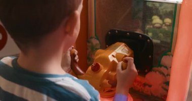 Küçük bir çocuk oyun makinesiyle etkileşime girer ve dikkatle kontrollere odaklanır. Sahne, kapalı bir eğlence salonunda oynayan bir çocuğun neşe ve konsantrasyonunu yakalıyor..