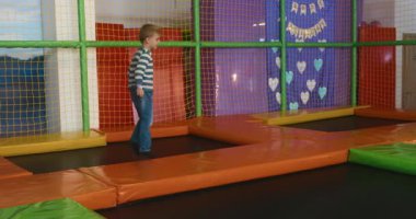 Genç bir çocuk renkli yastıklı bloklar ve güvenlik ağlarıyla çevrili canlı bir oyun alanında oynamaktan hoşlanıyor. Neşeli ortam eğlenceli ve aktif keşifleri teşvik eder..