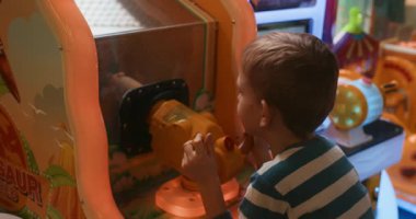 Genç bir çocuk dinazor temalı bir atari oyunuyla meşgul oluyor, odak ve heyecanla kolu çeviriyor. Sahne, atari salonunun canlı renklerini ve neşeli atmosferini yakalıyor..