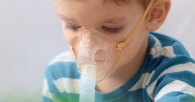 Çizgili gömlekli bir çocuk solunum tedavisi için nebulizör kullanıyor. Video, çocuğun bir maskeyle ilacı soluyarak ev sağlık hizmetlerini ön plana çıkardığını gösteriyor..